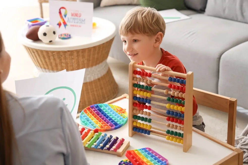 A smiling young boy using a colorful rainbow abacus during a therapy session