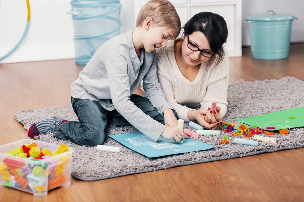 A mother and her young son drawing together with colorful chalk on the floor