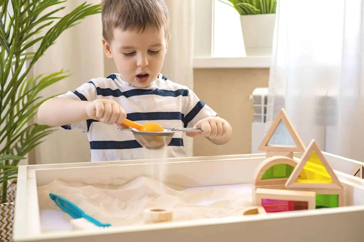 A young boy exploring a sensory sand tray with wooden shapes